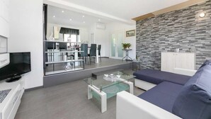 Ein modernes Wohnzimmer mit Glastisch, einer Couch und einem Fernseher.
