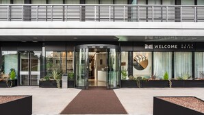 A modern hotel entrance with a revolving door, glass facade, and a welcome sign. - Welcome Hotel (Serravalle)
