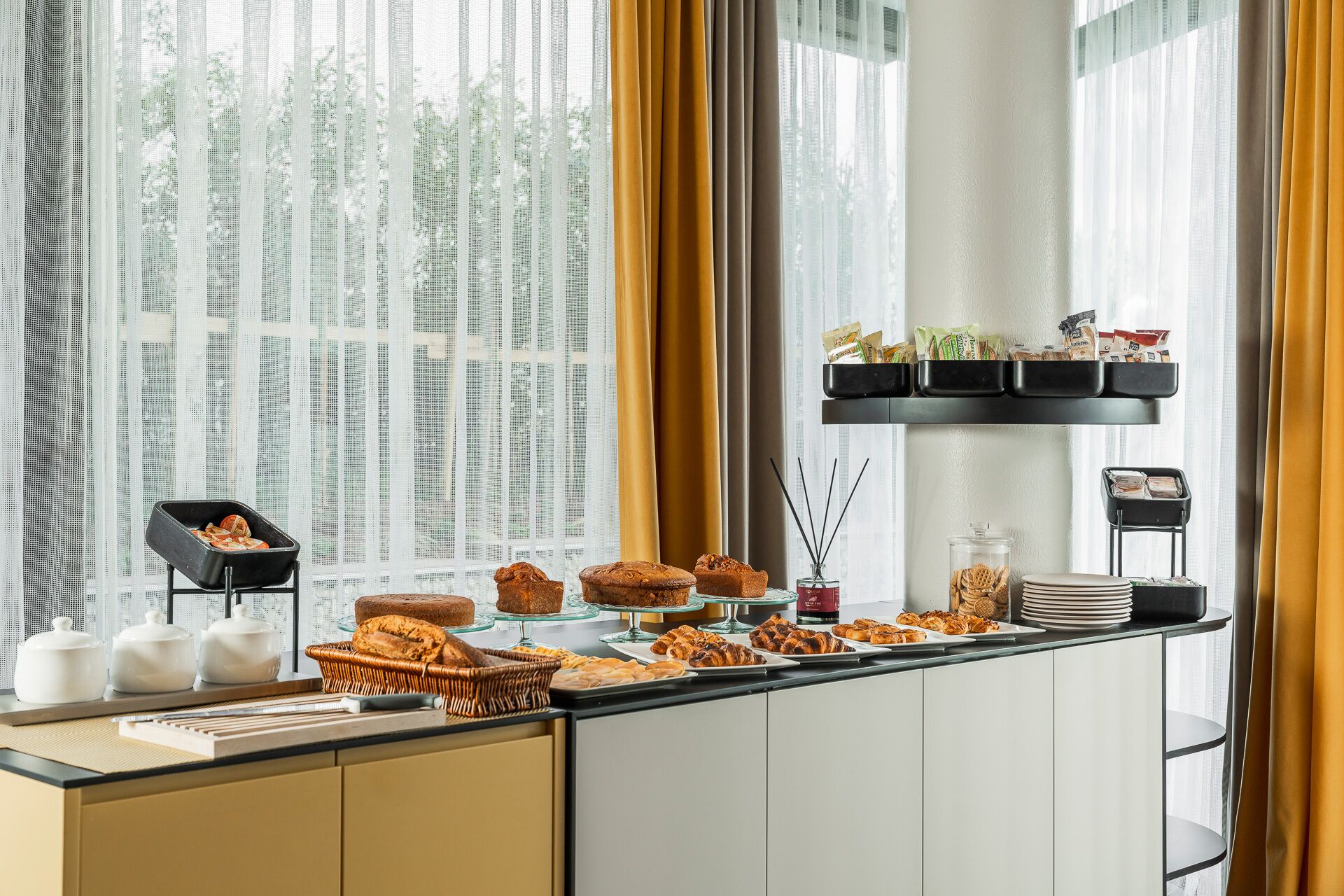 Un bufé de desayuno con diversos pasteles y pan, una estación de café y una repisa con aperitivos.