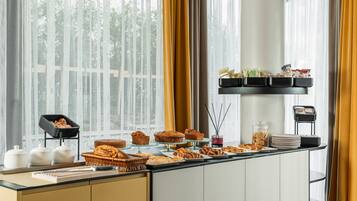Un bufé de desayuno con diversos pasteles y pan, una estación de café y una repisa con aperitivos.