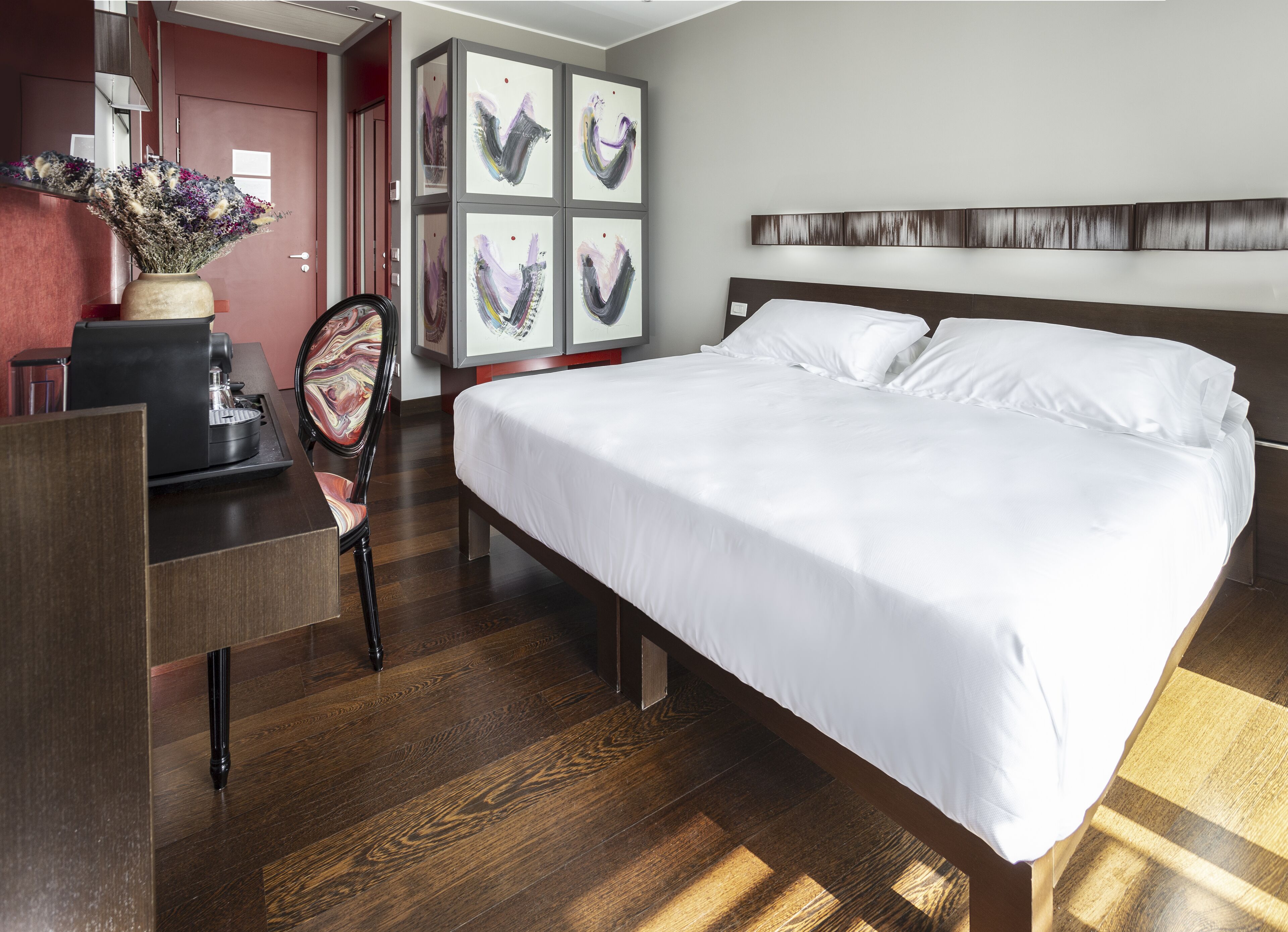 Una habitación de hotel con una cama grande, un escritorio con cafetera, una silla y obras de arte en las paredes.