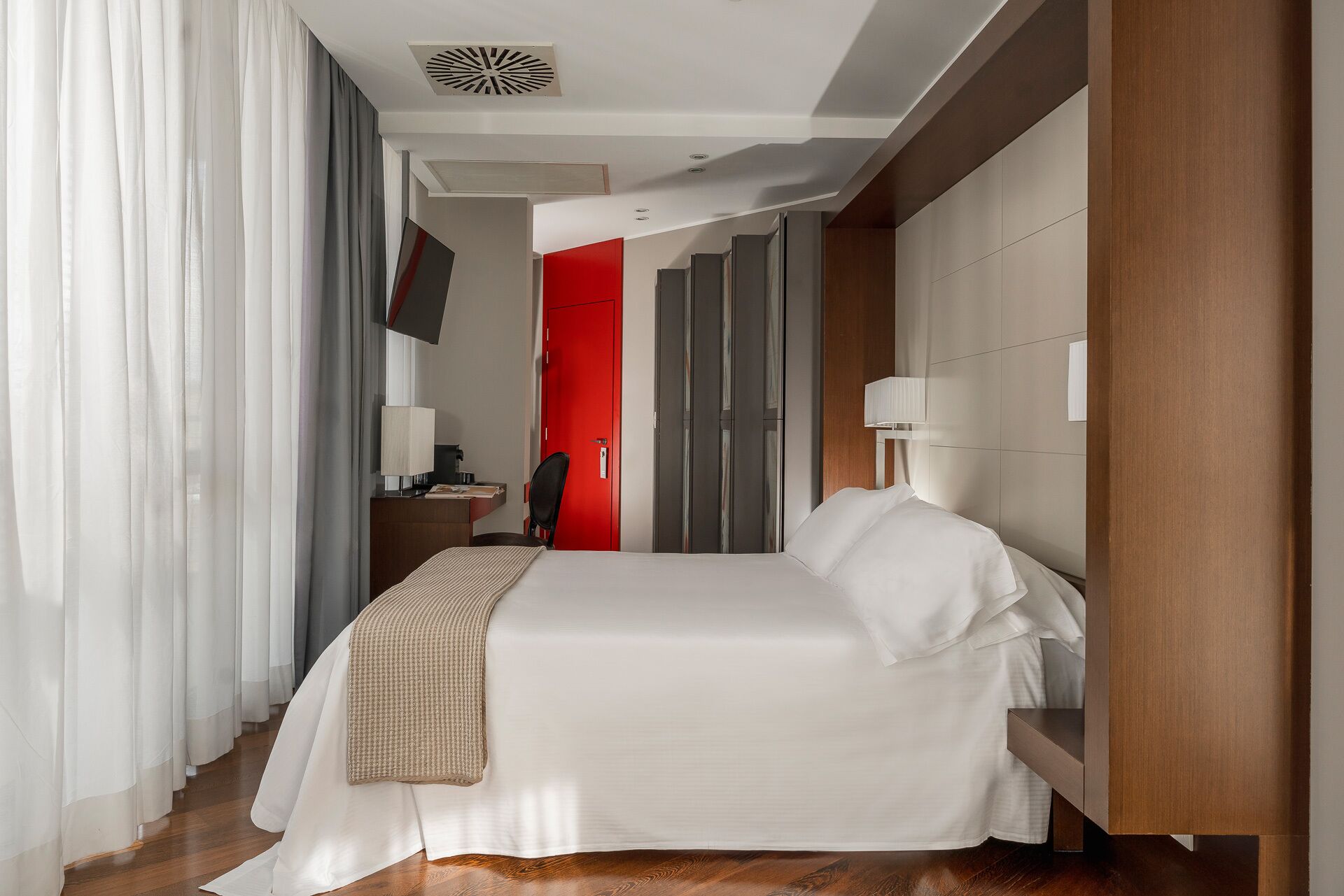 Una habitación de hotel con una cama, un escritorio, una silla, un televisor y una puerta roja.