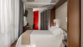 Una habitación de hotel con una cama, un escritorio, una silla, un televisor y una puerta roja.