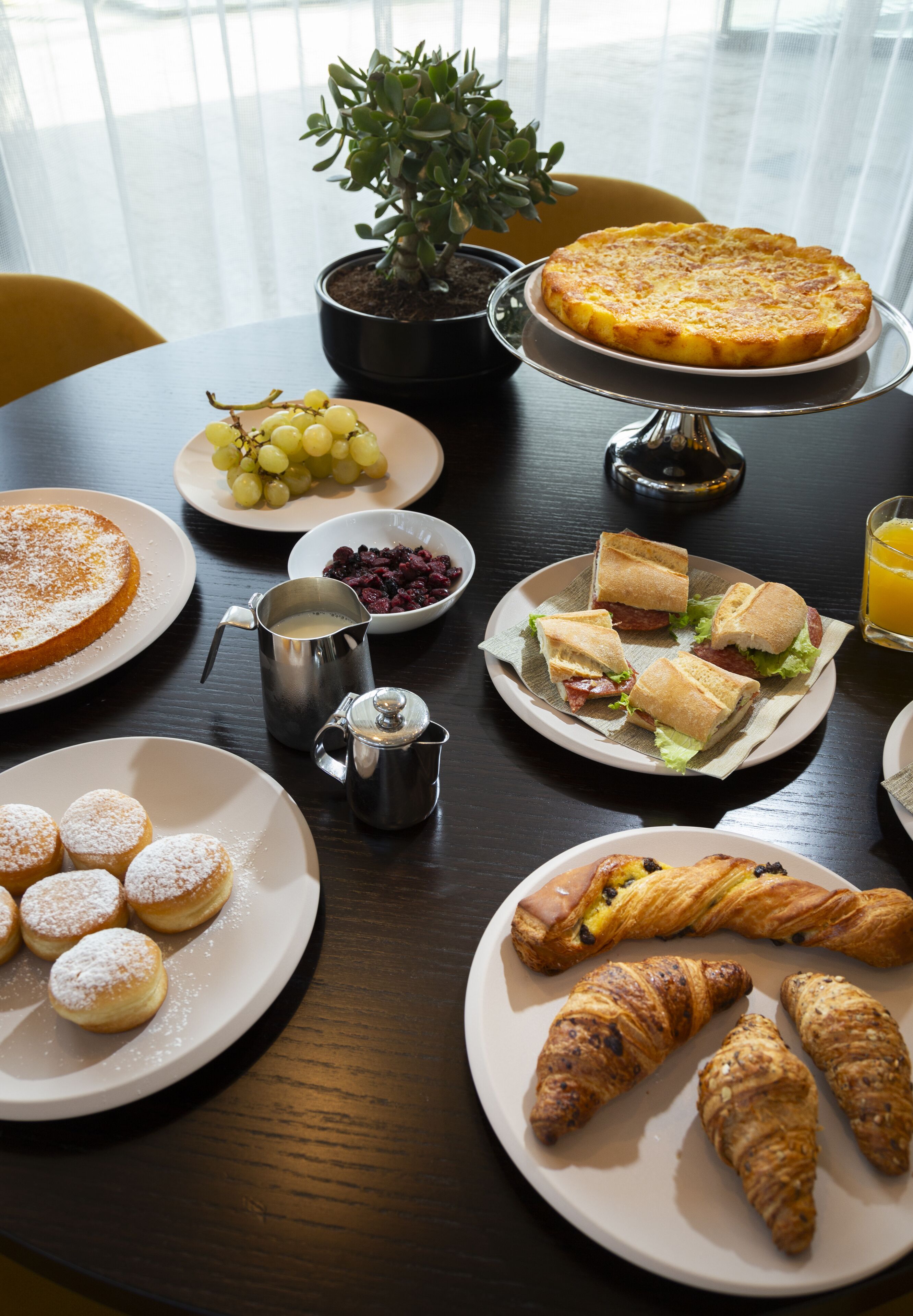 A breakfast table with plates of food, including a quiche, sandwiches, pastries, and a coffee pot.