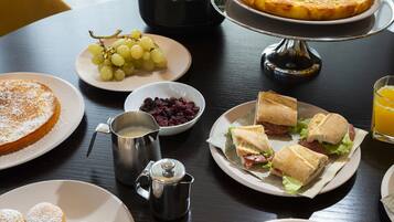 A breakfast table with plates of food, including a quiche, sandwiches, pastries, and a coffee pot.