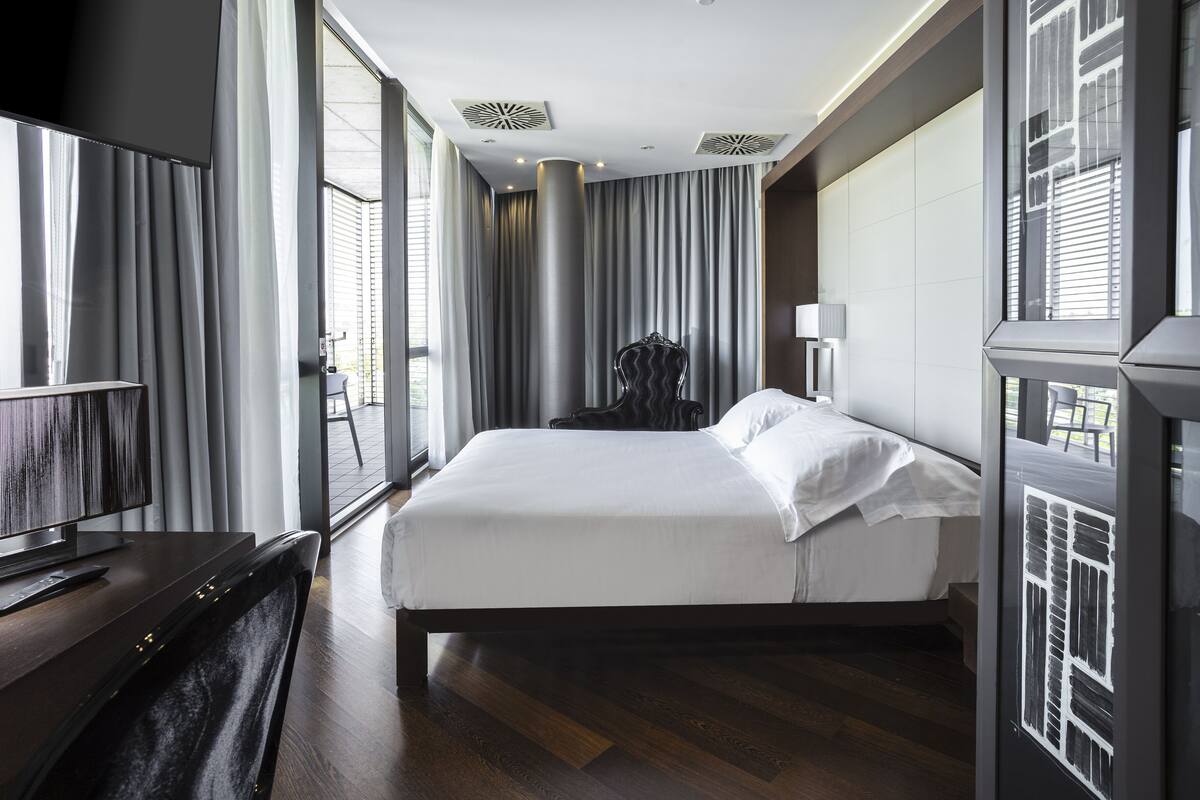 Ein modernes Hotelzimmer mit einem großen Bett, einem Flachbildfernseher und Blick auf die Stadt durch große Fenster.