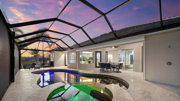 Ein moderner Poolbereich im Freien mit Glasdach, umgeben von einer Terrasse mit Sitzgelegenheiten und Blick auf den Sonnenuntergang.