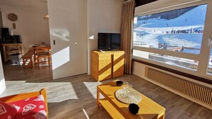 A modern living room with a large window offering a view of a snowy mountain landscape. - Charming Apartment Near Ski Lifts in Prapoutel, Sleeps 6, Balcony, TV, No Pets (Les Adrets-Prapoutel)