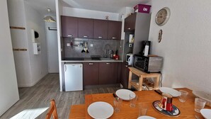 A compact kitchen with dark cabinets, a white refrigerator, a microwave, and a small dining table set for four. - Charming Apartment Near Ski Lifts in Prapoutel, Sleeps 6, Balcony, TV, No Pets (Les Adrets-Prapoutel)
