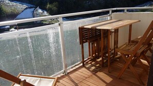 En træterrasse med et bord og stole, med udsigt over vandet.