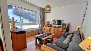 En hyggelig stue med et stort vindue, et træskab, en sofa og et fjernsyn.