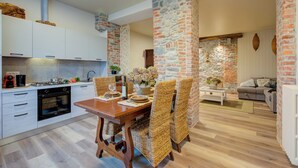 Une cuisine moderne avec des meubles blancs, un four encastré et un coin repas agrémenté de chaises en osier et d’une table en bois.