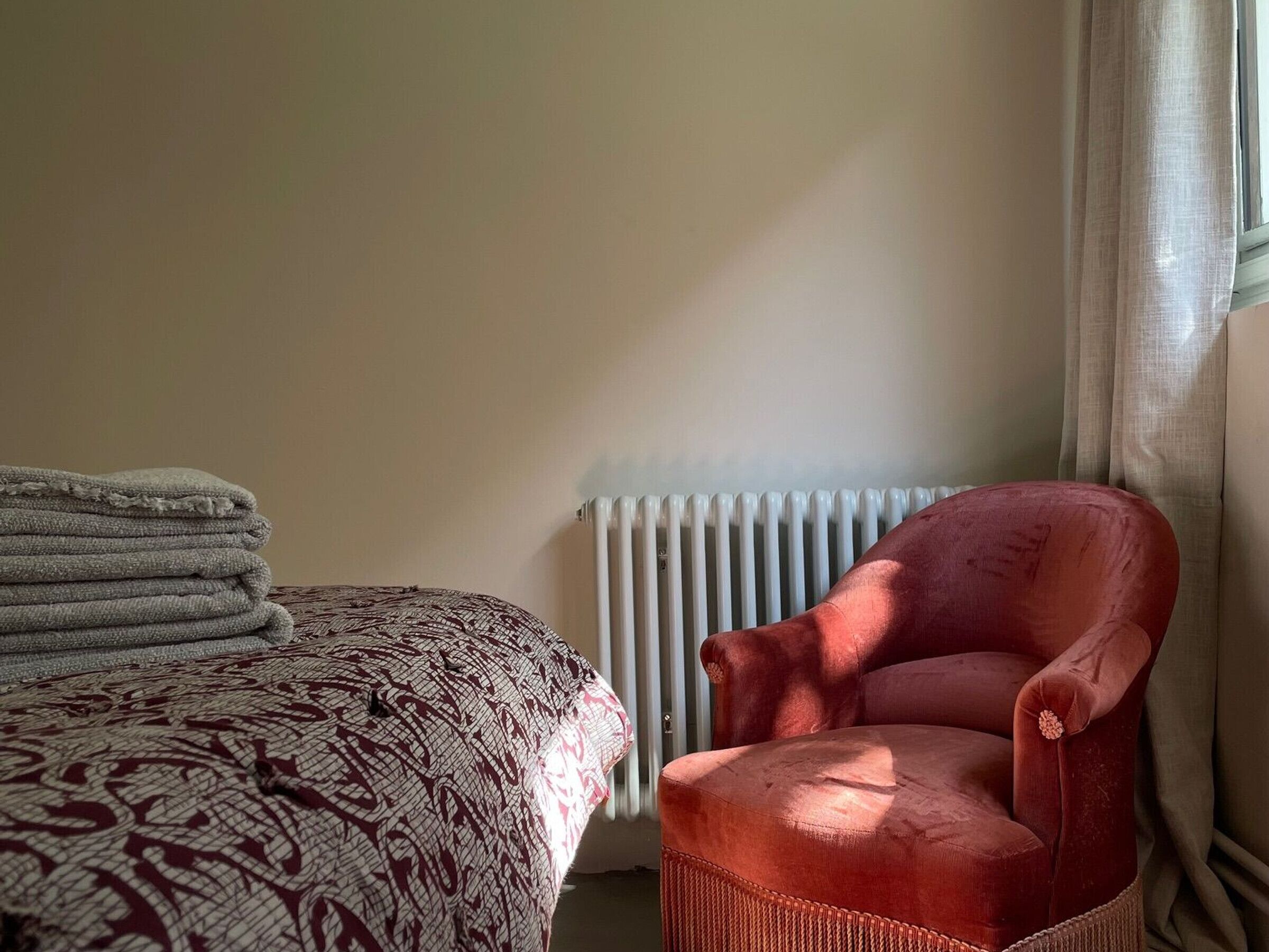 Una habitación con una cama, un sillón rojo y un radiador.
