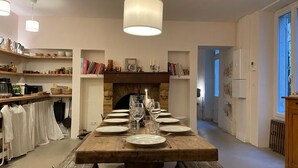 Un coin repas avec une table en bois dressée pour six personnes, une cheminée et une cuisine en arrière-plan.