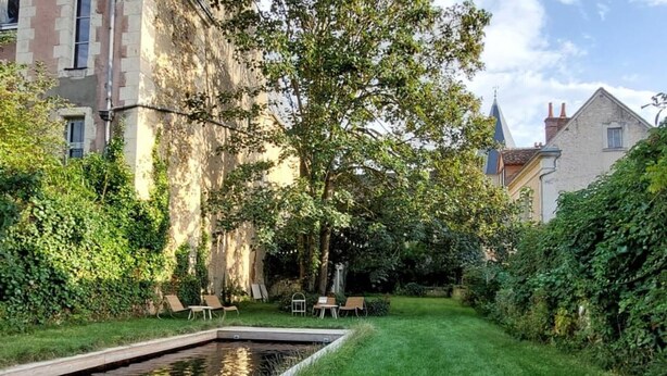 Une cour paisible avec une petite piscine, une végétation luxuriante et quelques chaises longues.