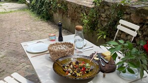 Une table dressée à l’extérieur, avec un saladier rempli de salade, du fromage et une bouteille d’eau.
