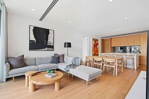 A modern living room with a grey sofa, a coffee table, and a dining area with wooden chairs and a white table.