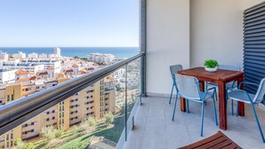 Ein Balkon mit Blick auf die Stadt und das Meer, ein Tisch mit Stühlen und ein Topfpflanze.