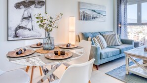 Ein modernes Wohnzimmer mit Essbereich, ausgestattet mit einem großen Fenster, einem blauen Sofa und einem Gemälde einer Frau mit Hut.