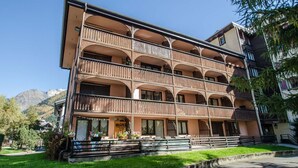 Un hotel de varios pisos con balcones, una entrada central y vistas a montañas al fondo.