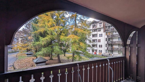 Un balcón con vista a un árbol y un edificio.