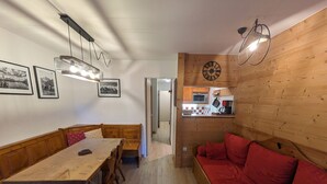 Un interior acogedor con una mesa de comedor de madera, bancos, un sofá rojo y una cocina visible a través de un vano abierto.