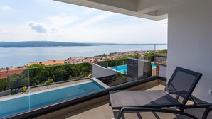 A balcony with a glass barrier overlooking a swimming pool and a coastal town. - Lovely home in Crikvenica (Crikvenica)