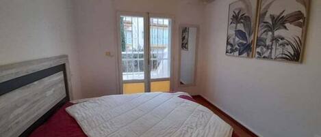 Un dormitorio con una cama, una colcha roja, una lámpara en el techo, una ventana y una puerta.