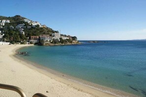 A beach with clear water, a sandy shore, and buildings on a hillside.