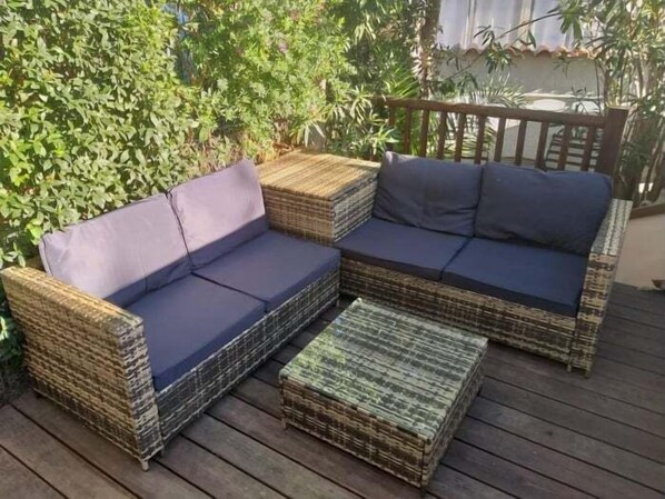 A wicker sofa with cushions and a matching ottoman on a wooden deck.