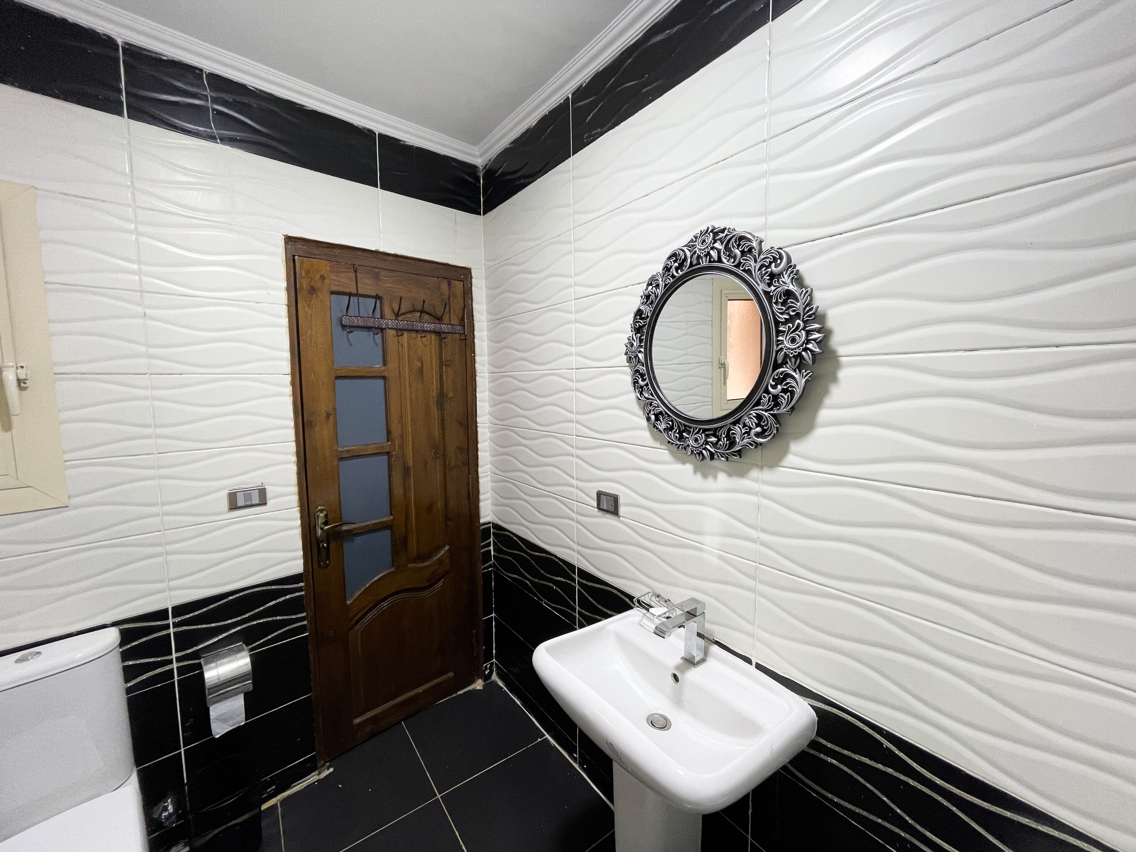 A bathroom with a wooden door, a white sink, and a decorative mirror.