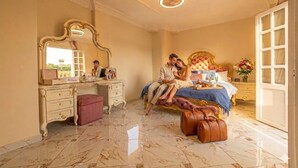 A bedroom with a bed, a vanity, a mirror, a dresser, and a suitcase. - Chez l'ami hotel (Giza)
