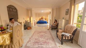 Ein Hotelzimmer mit Bett, Essbereich mit Tisch für zwei Personen, Sitzgelegenheit mit Sessel und Blick durch das Fenster.