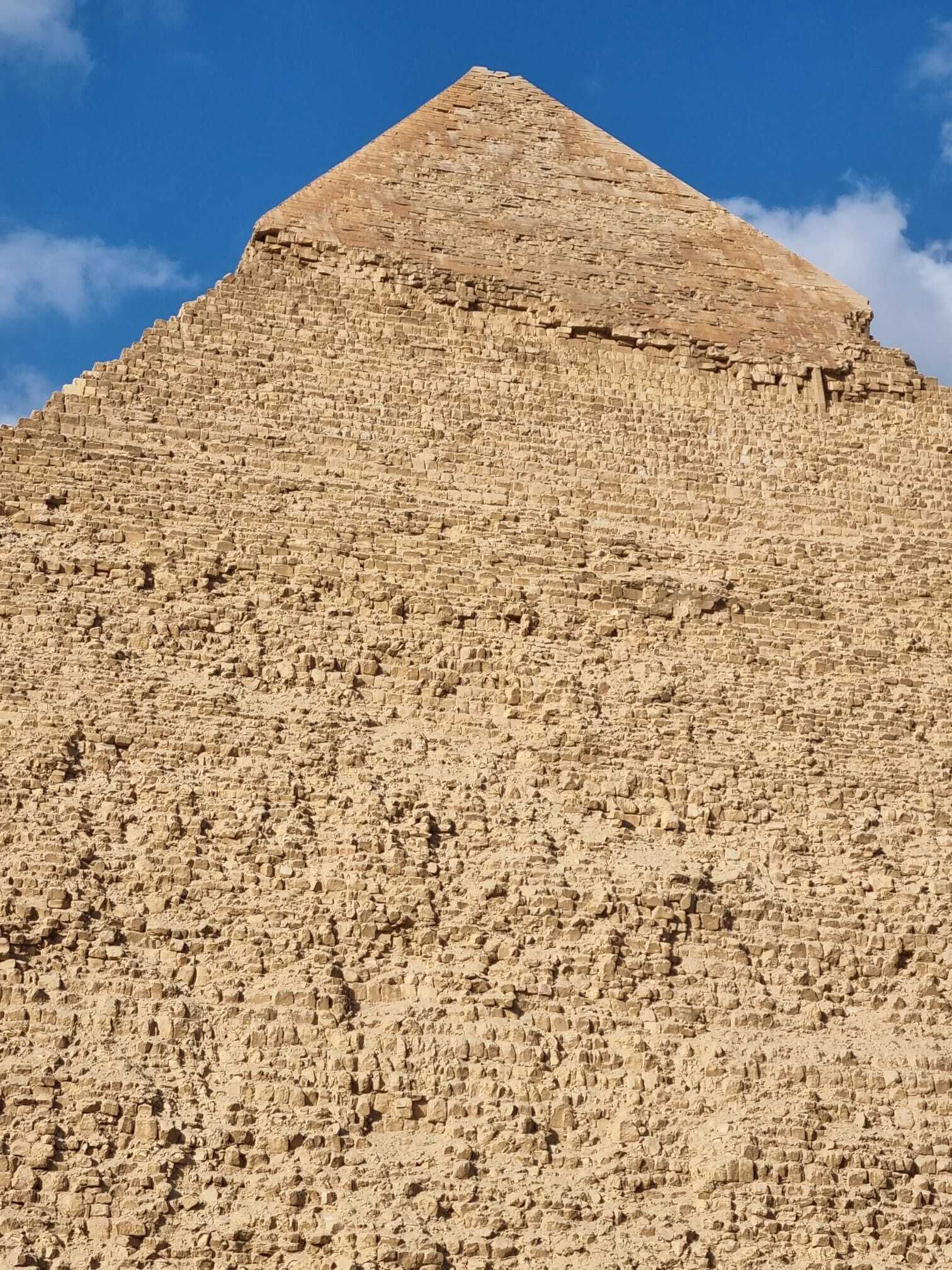 A large, ancient stone pyramid with a broad base and a narrow top, set against a clear blue sky.