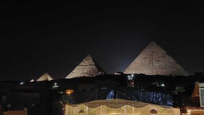 A nighttime view of a pyramid-shaped building with a large, illuminated structure in the foreground. - Chez l'ami hotel (Giza)