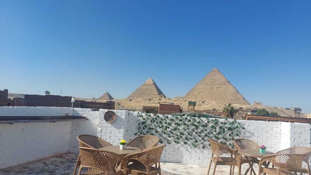 A rooftop terrace with wicker furniture and a view of the pyramids. - Chez l'ami hotel (Giza)