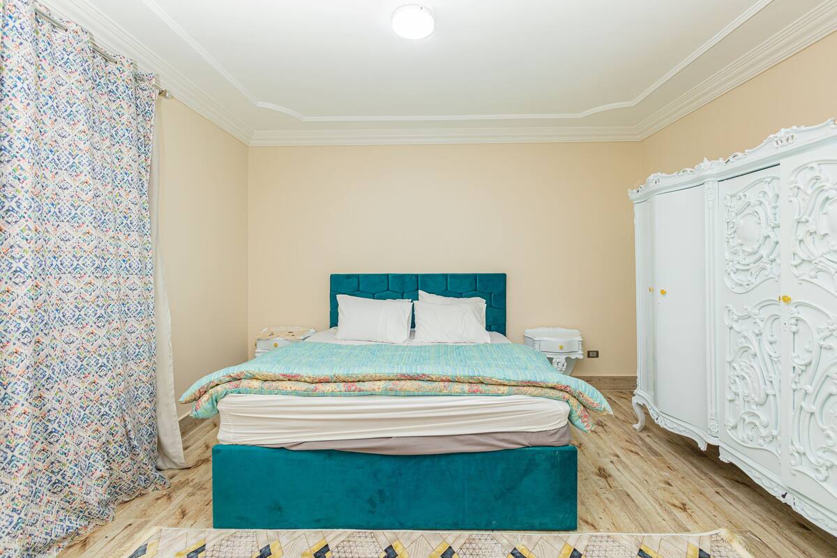 Un dormitorio con cama, armario blanco y cortina estampada.