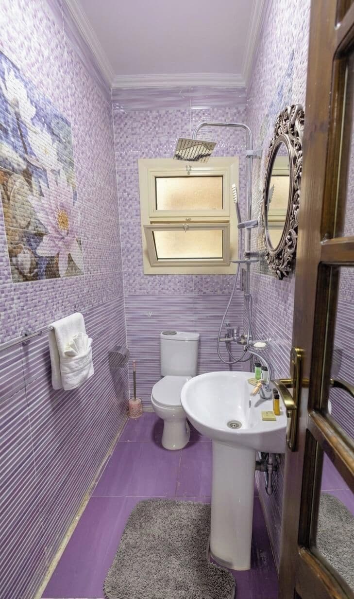 Un baño con inodoro, lavamanos y espejo con marco decorativo.