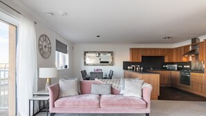 Un salon moderne avec un canapé rose, une table à manger et un coin cuisine doté de meubles en bois et d’un plan de travail noir.