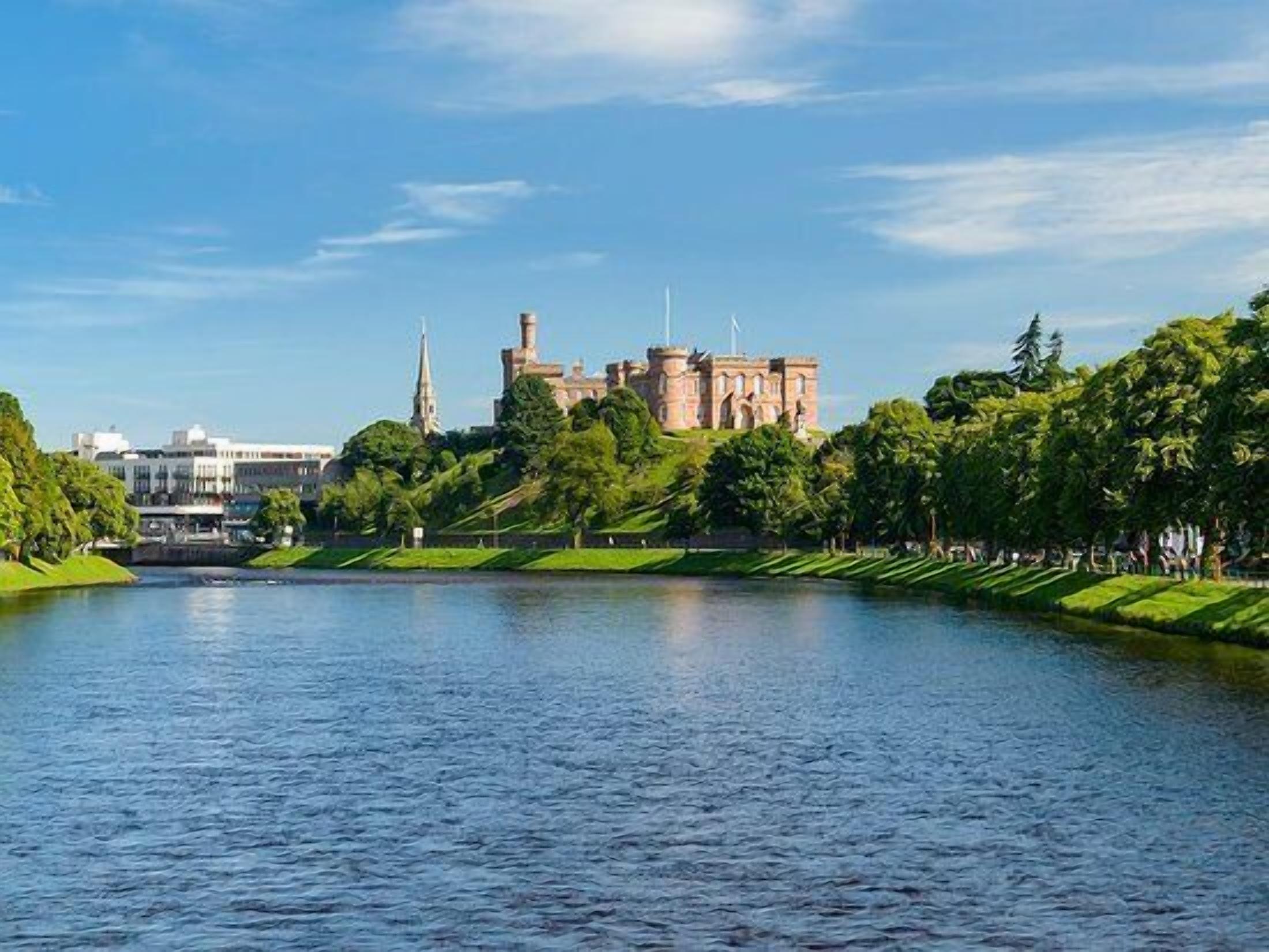 A castle-like building with a tower, surrounded by a park and a body of water.