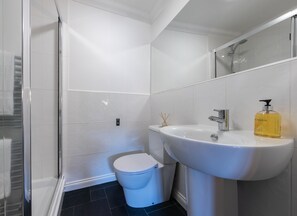 A modern bathroom with a white sink, toilet, and glass shower enclosure. - Luxury Riverside Apartment - Sleeps 8 (Inverness)