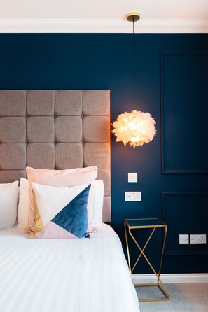 A neatly made bed with a tufted headboard, a decorative hanging light fixture, and a small bedside table with a geometric design.