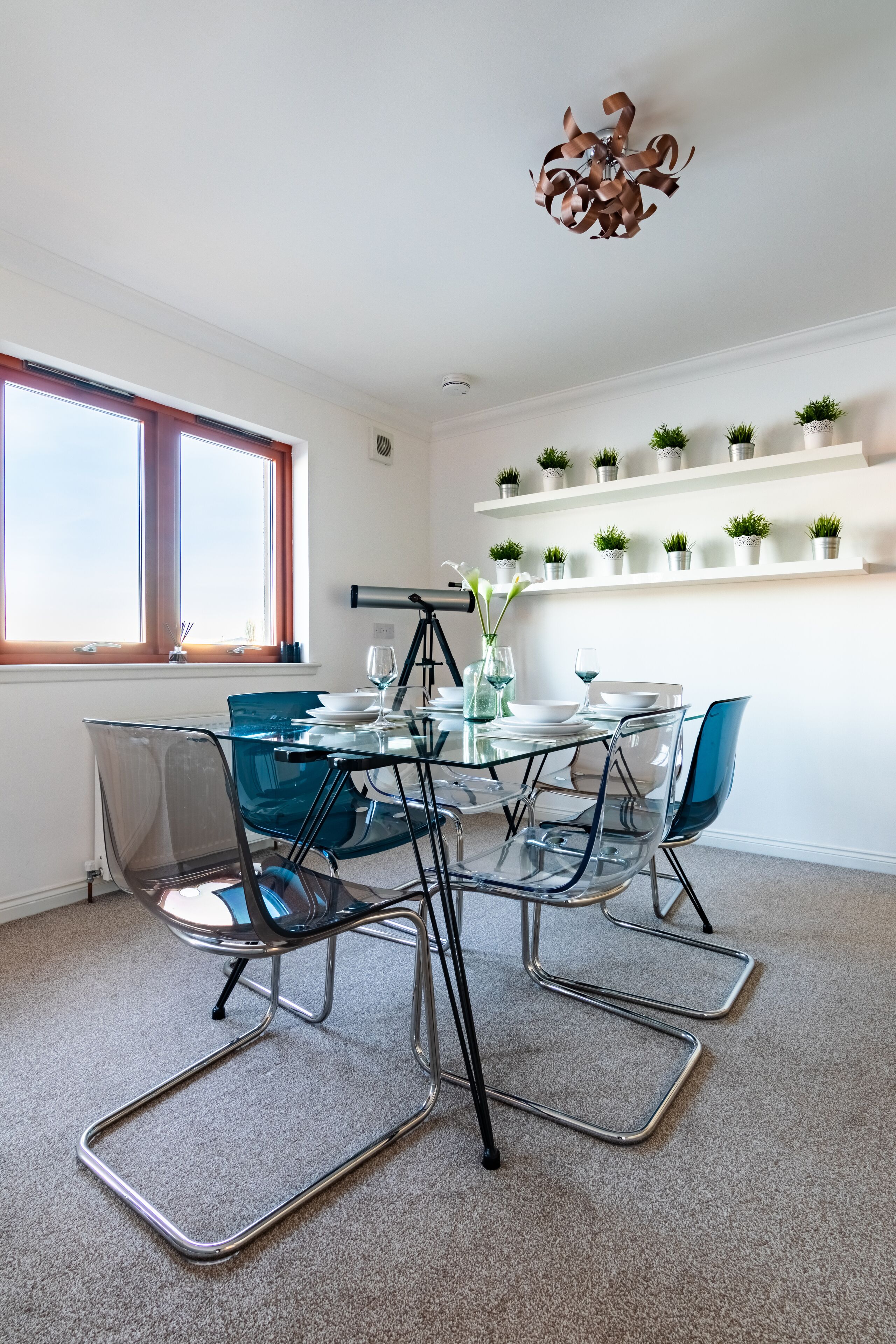 A modern dining area with a glass table, metal chairs, and a telescope on a tripod.
