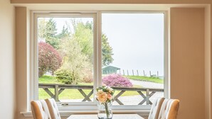 A dining area with a table and four chairs, a window with a view of a garden and a fence, and a vase with flowers on the table. - Essich Park - 2BR - Hot Tub - Sleeps 4 (Inverness)
