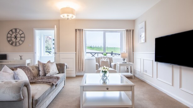 A living room with a sofa, coffee table, and TV. There is a window with a view of a fence and greenery. - Essich Park - 2BR - Hot Tub - Sleeps 4 (Inverness)
