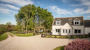 A two-story house with a gravel driveway, a wooden fence, and a gazebo. - Essich Park - 2BR - Hot Tub - Sleeps 4 (Inverness)