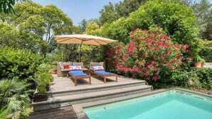 Area piscina con due lettini, un ombrellone beige e una piccola piscina.