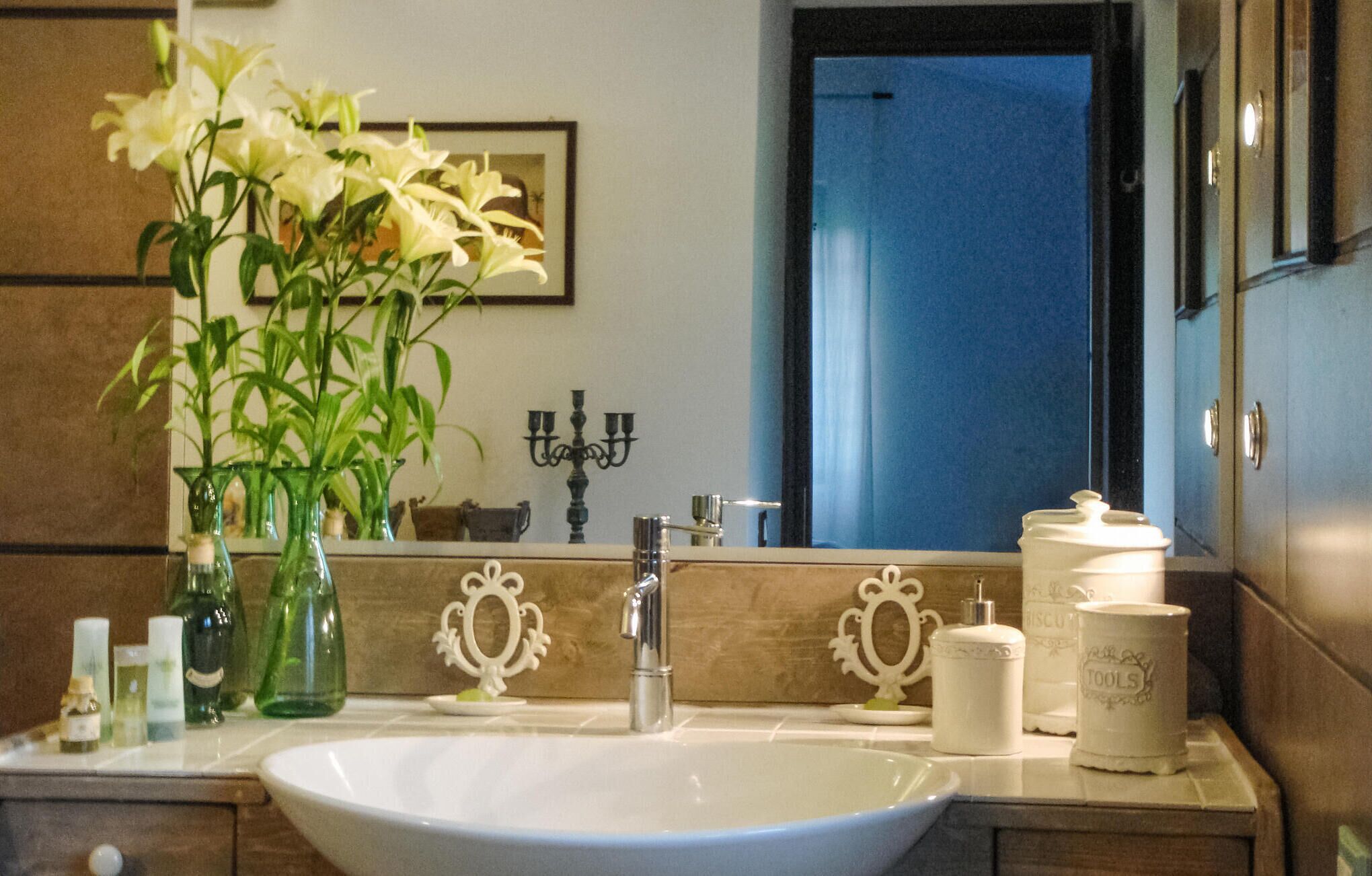 A bathroom with a white sink, a mirror, a vase with flowers, and toiletries on the counter.
