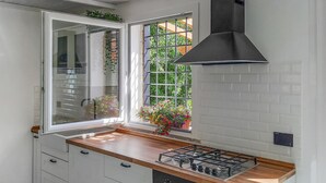 Cucina con piano cottura a gas, mobili bianchi, una finestra vista su vegetazione e cappa aspirante nera.