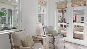 Ein Zimmer mit zwei Polstersesseln auf Holzfüßen, einem kleinen Beistelltisch mit Lampe und Blick auf einen Balkon mit Korbmöbeln.